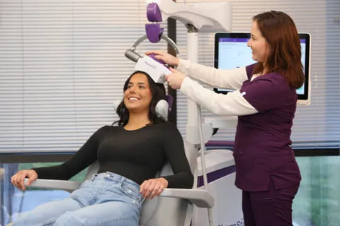 A clinician positioning a TMS device on a smiling patient exploring How many sessions of TMS are needed?